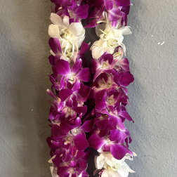 Purple and white orchid lei hanging against a gray wall