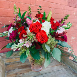 Bouquet of red roses, white blooms, and pink lilies in a glass vase