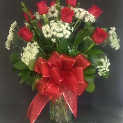 Tall arrangement of red roses and white filler flowers in a clear glass vase with a large red bow.