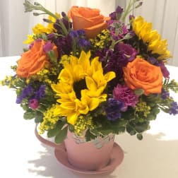 Bouquet of orange roses and yellow sunflowers in a pink mug-style vase