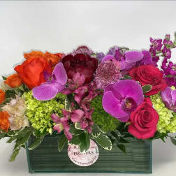 Mixed bouquet of roses, orchids, and purple blooms in a rectangular vase