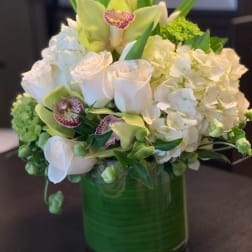 White roses, hydrangeas, and orchids in a green glass vase