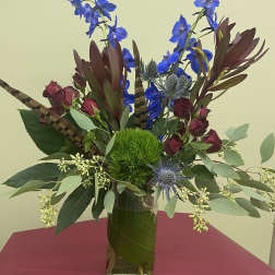 Tall vase arrangement with blue flowers, burgundy roses, and a green moss ball