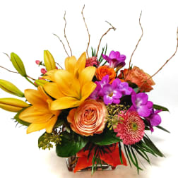 Colorful bouquet with yellow lilies, orange roses, and purple flowers in a glass vase