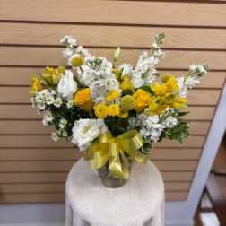 Yellow and white flower arrangement in a glass vase with a ribbon