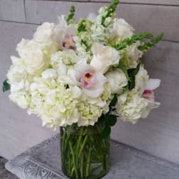 White floral arrangement in a glass vase with pink orchid accents