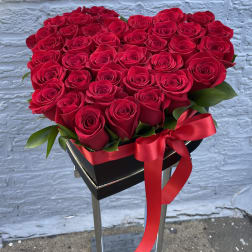 Heart-shaped arrangement of red roses with a red ribbon on a black stand