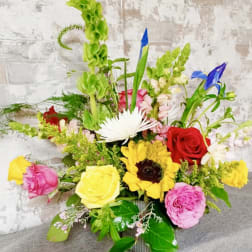Colorful mixed flower arrangement in a metal container with roses and sunflowers