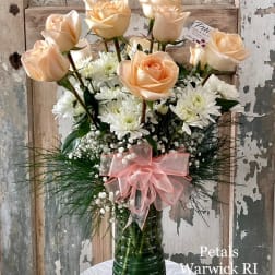 Peach roses and white daisies in a tall green glass vase with a pink bow