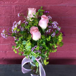 Pink roses in a glass vase with purple filler flowers and a ribbon