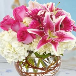 Pink roses and lilies arranged with white hydrangeas in a glass bowl vase