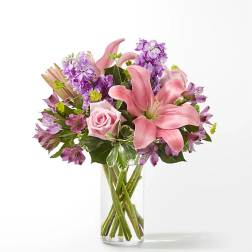 Pink lilies and roses with purple flowers in a clear glass vase