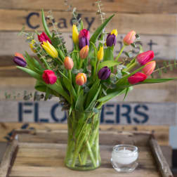 Colorful tulips in a glass vase with a small candle beside it