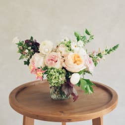 Pastel floral arrangement in a clear glass vase on a wooden table