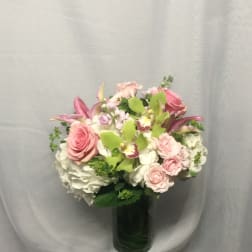 Round arrangement of pink roses, green orchids, and white hydrangeas in a clear glass vase