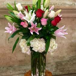 Tall bouquet of pink and red roses with lilies in a glass vase