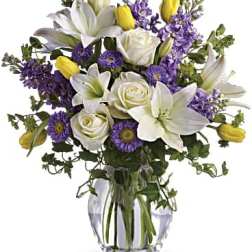 Bouquet of white lilies, roses, and purple flowers in a glass vase