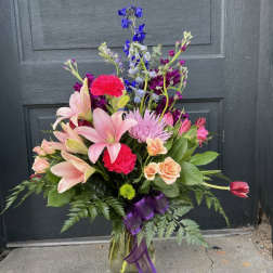 Mixed bouquet of pink lilies, roses, and purple flowers in a glass vase
