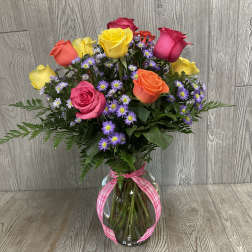 Mixed bouquet of colorful roses and purple daisies in a glass vase