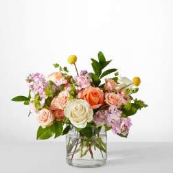 Pink and peach roses in a clear glass vase with small purple flowers