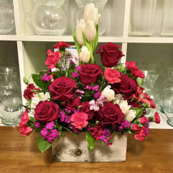 Mixed bouquet of red roses, pink carnations, and white tulips in a rectangular vase