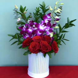 Red roses and purple orchids in a striped white box