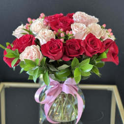 Bouquet of red and pale pink roses in a glass vase with a pink ribbon