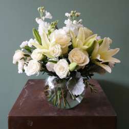White lilies and roses arranged in a round glass vase