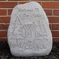 Carved stone plaque with a cabin, trees, and bears against a brick wall