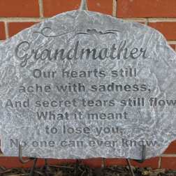 Gray memorial stone engraved for grandmother against a brick wall