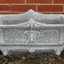 Ornate gray stone planter box against a brick wall