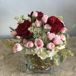 Pink and red roses arranged in a clear square vase