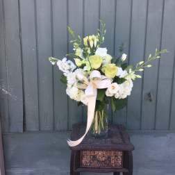 White and pale green floral arrangement in a glass vase with a ribbon