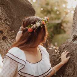 Woman wearing a floral crown and white dress standing by a tree