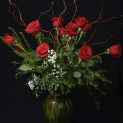 Red roses arranged in a glass vase with curly branches