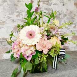 Pastel flower arrangement in a green glass vase with a striped ribbon