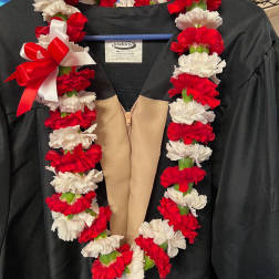 Red and white carnation lei draped over a black graduation gown