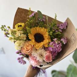Hand-tied bouquet with a sunflower, roses, and pastel blooms in brown paper