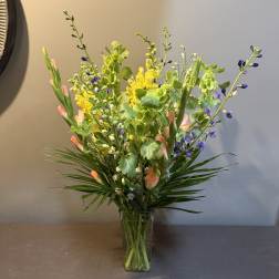 Tall mixed bouquet in a clear glass vase with yellow, purple, and peach blooms