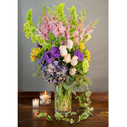 Tall mixed bouquet in a glass vase with candles beside it
