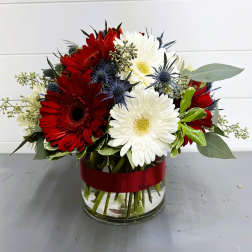 Red and white gerbera daisies in a glass vase with a red ribbon