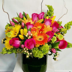 Bright mixed bouquet with pink roses, orange gerberas and yellow blooms in a dark green vase