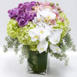 Purple and pink roses with white orchids in a clear glass vase