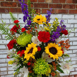 Mixed bouquet with sunflowers, red carnations, and purple blooms in a patterned vase