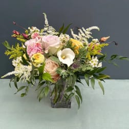 Mixed bouquet of pastel roses, calla lily, and white filler flowers in a glass vase
