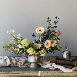 Mixed flower arrangement in a silver vase with peach, white, and blue blooms