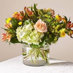 Mixed bouquet of peach roses, white hydrangea, and yellow flowers in a glass vase