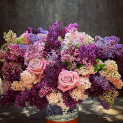 Pink roses in a decorative vase surrounded by purple and lavender blossoms