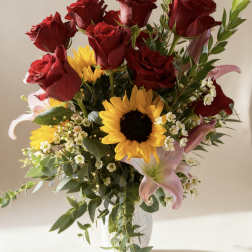 Bouquet of red roses, sunflowers, and pink lilies in a clear vase