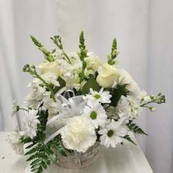 White floral arrangement in a basket with daisies and roses